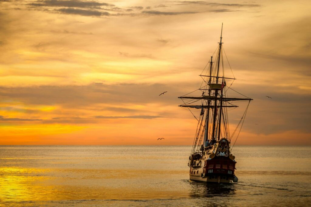 A majestic pirate ship sails into the serene waters at sunset, casting a dramatic silhouette.